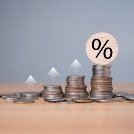 Percent sign on a wooden cube with row of coins in idea for FED consider interest rate hike, inflation concept, white graph arrow, world economics, and inflation control, Money and budget management